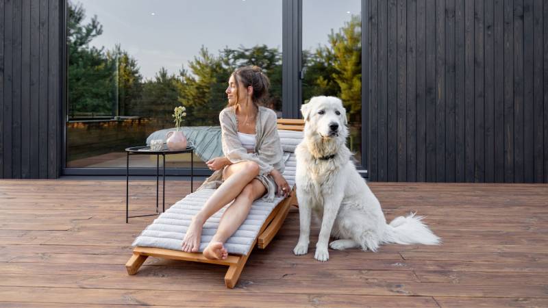 A woman relaxing on a wooden deck with her large white dog, illustrating a pet-friendly exterior finish that withstands the activity of furry companions.